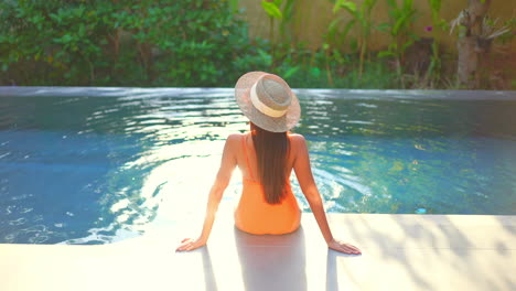 Back-view-of-woman-sitting-on-pool-edge-with-sunlight-reflecting-on-water