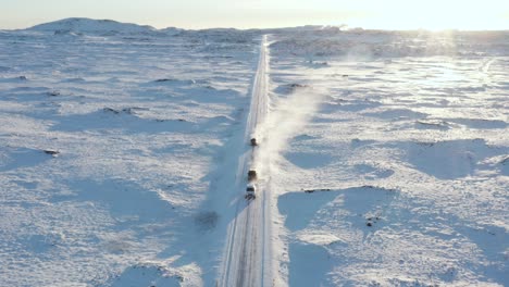 Cars-traveling-on-snow-road-in-Iceland-during-bright-midday-sun,-aerial