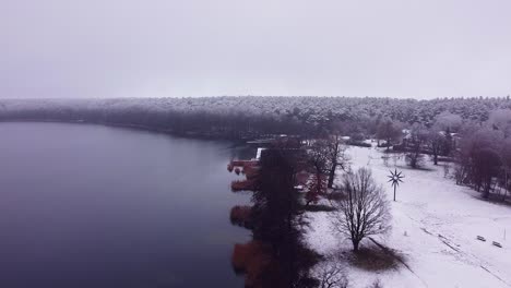 Flying-from-above-the-shore-covered-with-a-thin-layer-of-snow-over-a-calm-lake