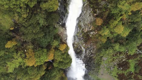 Idyllic-Snowdonia-mountain-range-Aber-falls-waterfalls-national-park-aerial-view-birds-eye-over-cliff-edge-tilt-up