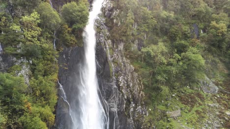 Idyllic-Snowdonia-mountain-range-Aber-falls-waterfalls-national-park-aerial-pull-back-view