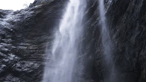 following-slow-motion-of-a-waterfall-inside-massive-glacier-canyon,-rain-drops-falling-through-frame-with-wet-stones-background