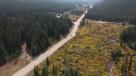 Aerial-View-of-a-Lonely-Car-on-Road-in-Rural-Countryside-Valley-in-Autumn-Colors-Surrounded-With-Green-Coniferous-Forest,-Drone-Shot