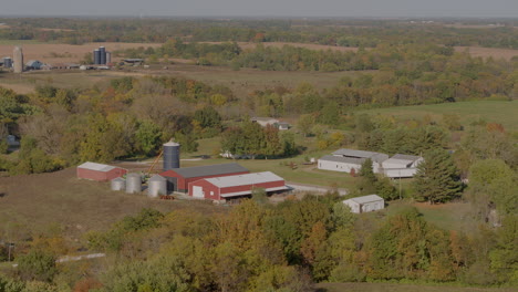 Aerial-of-a-farm-in-the-midwest-surrounded-by-beautiful-autumn-trees-with-pull-away-over-a-harvested-corn-field
