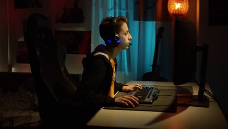 A-teenage-boy-in-headphones-playing-an-online-computer-game,-communicating-with-players,-happy-and-excited