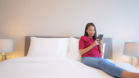 Feet-up-and-sitting-propped-up-with-pillows-a-young-woman-focuses-on-her-smartphone-screen