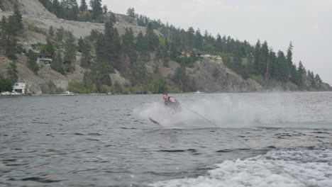 Man-water-skiing-behind-boat-on-mountain-lake-with-big-water-splash