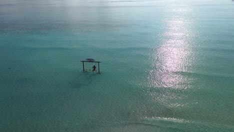 Luftaufnahme-Einer-Einsamen-Frau,-Die-In-Einem-Seichten-Türkisfarbenen-Wasser-Auf-Den-Malediven-Schwingt