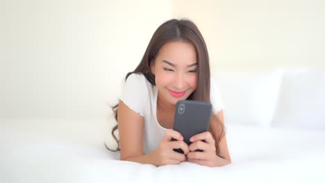 Schönes-Erwachsenes-Mädchen,-Das-Mit-Dem-Smartphone-Interagiert,-Während-Es-Auf-Dem-Bett-Liegt