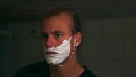 Young-man-shaving-beard-with-shaving-foam-and-a-razor