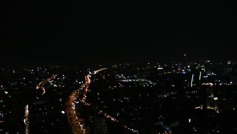 Panoramablick-Auf-Die-Skyline-Einer-Stadt-In-Der-Nacht-Mit-Wolkenkratzern-Und-Stark-Befahrener-Autobahn,-Die-Im-Dunkeln-Leuchten