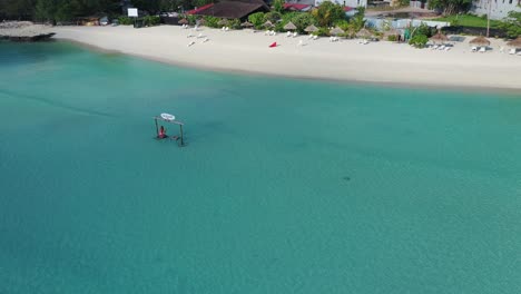 Einsame-Frau-Auf-Schaukel-Im-Seichten-Wasser-Vor-Weißem-Sandstrand-Auf-Malediven-Gulhi-Island,-Exotisches-Tropisches-Urlaubsziel,-Drohnenaufnahme