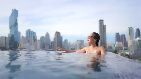 Girl-in-Infinity-Swimming-Pool,-Spa-with-Urban-Skyline-Background