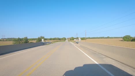 POV-driving-over-a-bridge-and-past-mature-corn-fields-and-farmyards-in-rural-Iowa-on-a-sunny-early-autumn-day