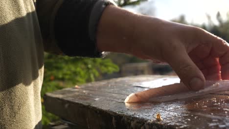 Caucasian-man's-hands-prepare-a-fish-fillet-outdoors-in-sun,-close-up