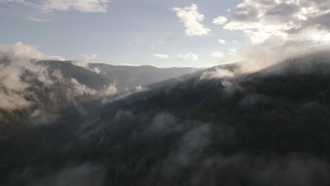 4K-scenic-aerial-footage-of-a-mountain-top-covered-in-steam-clouds-and-fog-being-lighted-by-the-sunrise-4K