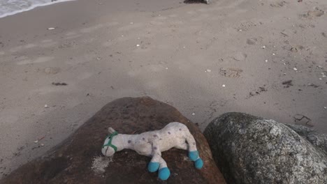 Forgotten-child-toy-left-on-the-rock-on-the-beach,-tilt-shot