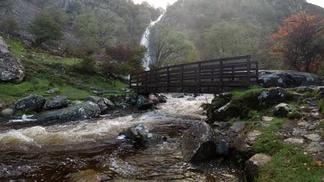 Waterfall-rocky-river-flowing-water-slow-motion-cascades-under-wooden-bridge-in-national-park