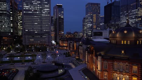 High-above-aerial-view-out-on-famous-Tokyo-Station-at-night-with-commuters-moving-around-and-skyscrapers-in-backdrop