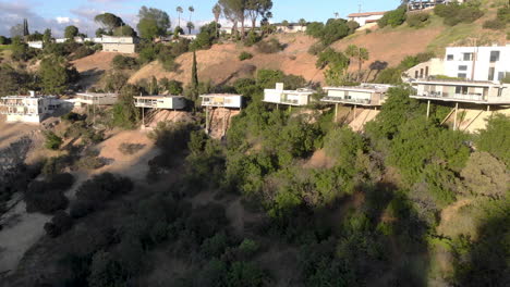 Aerial-flyby-of-homes-on-stilts-hanging-off-cliffs-of-a-mountain-overlooking-a-valley-city