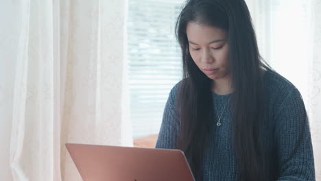 Asian-American-girl-at-home,-typing-on-laptop,-slow-motion