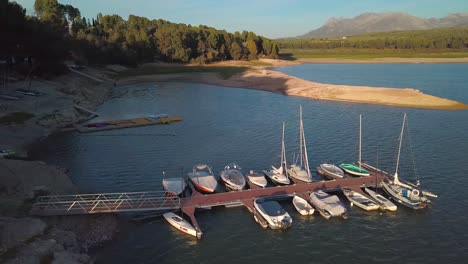 Toma-Aérea-Sobre-Un-Pequeño-Muelle-Con-Barcos-En-Un-Lago-De-Andalucía,-España