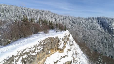 Drone-winter-mountain-view-of-a-man-going-for-a-sunny-hike-in-the-snow