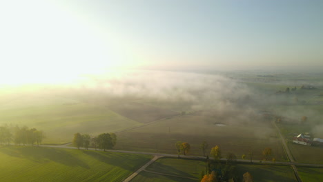 Luftflug-über-Wunderschönes-Ländliches-Ackerland-Mit-Niedrigen-Nebelwolken-Bei-Sonnenaufgang