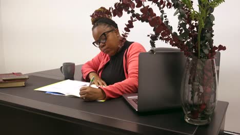 Mujer-De-Negocios-Negra-Con-Anteojos-Escribiendo-En-Un-Escritorio-En-La-Oficina-Vestida-Con-Atuendo-De-Negocios