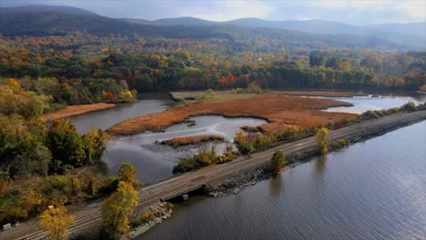 a-scene-with-a-river,-train-tracks,-marshland-swamps,-mountains,-hills,-and-autumn-foliage