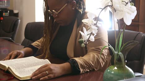Black-woman-wearing-glasses-reading-bible-in-a-office-space,-comfort,-relaxation-in-God's-word