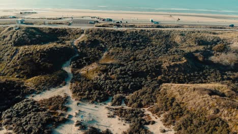 Aerial-birdseye-above-sandy-dune-terrain-tilt-up-to-coastal-ocean-road-horizon