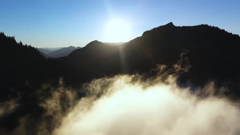 Sol-Matutino-Sobre-Picos-Montañosos-Y-Nubes-Sobre-El-Valle,-Vista-Aérea-Cinematográfica
