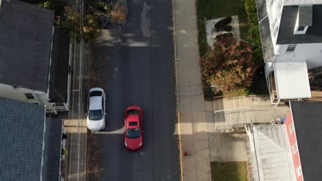 Aerial-tilt-down-as-red-car-passes-by-homes-with-American-flag-flying-in-breeze