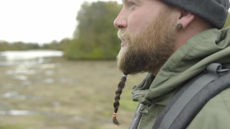 Close-up-shot-of-bearded-man-with-nose-piercing-and-backpack-during-nature-adventure-trip-in-wilderness