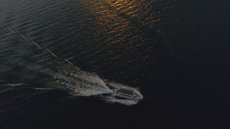 Aerial-shot-of-large-boat-moving-at-high-speed-across-Lago-Di-Garda-in-warm,-soft-sunset-light