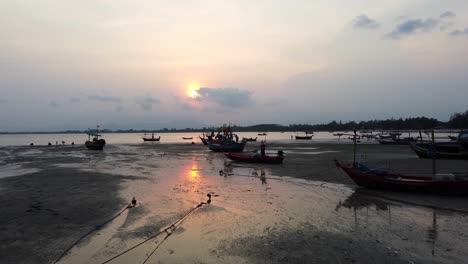 AERIAL:-Low-shot-of-Asian-style-Fishing-Boats-stranded-at-low-tide-on-the-coast-of-bay-at-Sunset
