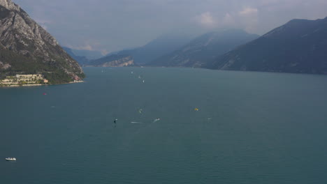 Vista-Aérea-De-Varias-Personas-Divirtiéndose-Haciendo-Kitesurf-Y-Windsurf-En-El-Lago-De-Garda,-Italia