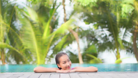 While-still-in-the-pool,-a-young-woman-leans-her-chin-on-her-arms-on-the-edge-of-a-swimming-pool