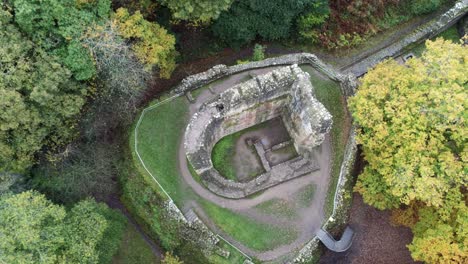 Aerial-view-above-Ewloe-castle-abandoned-ruins-hidden-in-Autumn-woodland-birdseye-rotating-left