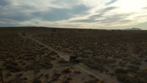 Aerial-view-of-an-off-road-vehicle-driving-along-a-dusty-desert-trail-at-dusk