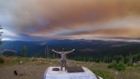 Man-on-top-of-van,-hands-up-during-wildfire-sunset,-frame-rate-59