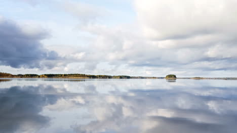 Pan-of-lake-water-reflecting-cloudy-sky-and-distant-forested-islands