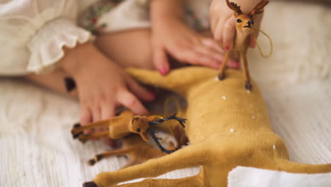 Slow-motion-of-little-girl-in-Christmas-dress-playing-with-deer-toy-figurines---Close-up-shot