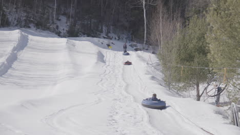Children-snow-tubing,-riding-rope-tow-uphill-on-sunny-winter-day