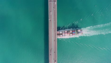 Large-Container-Ship-passing-under-a-bridge-with-traffic-in-Hong-Kong-bay,-Aerial-view