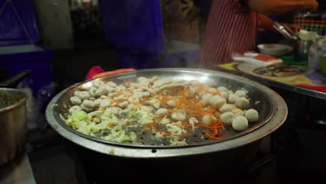 Slow-motion:-chef-cooking-vegetables-and-meat-in-huge-paella-pan-at-outdoor-night-food-market:-close-up