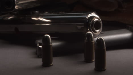 Pistol-stacked-on-cartridge-on-table-as-bullets-drop-nearby,-slow-pan