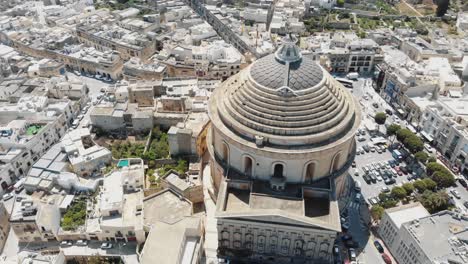 A-wide-view,-aerial-4k-drone-footage,-circling-the-Mosta-Rotunda-Dome,-a-Roman-Catholic-church,-and-the-surrounding-city-blocks-of-Malta