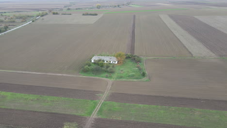 Brown-bare-farmland-in-off-season-surrounds-large-rural-white-farmhouse-drone